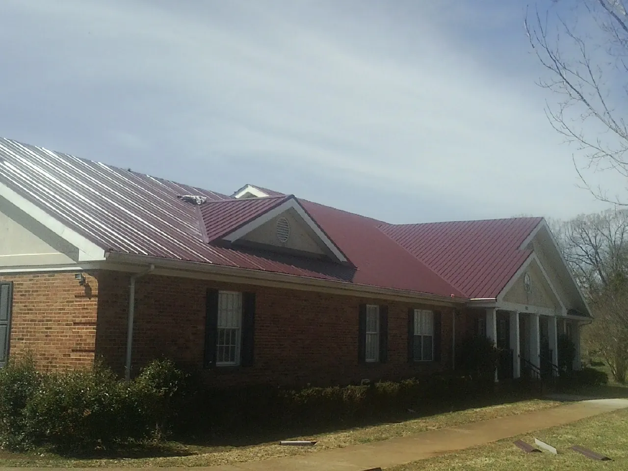 Red metal roof with gabled entries on a long brick building, from a Hail Damage Roof Repair job in The Villages