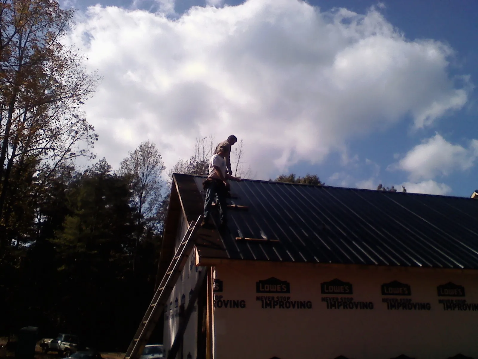 Roofer fastening dark metal panels high against a cloudy sky, from a Roof Inspection job in The Villages
