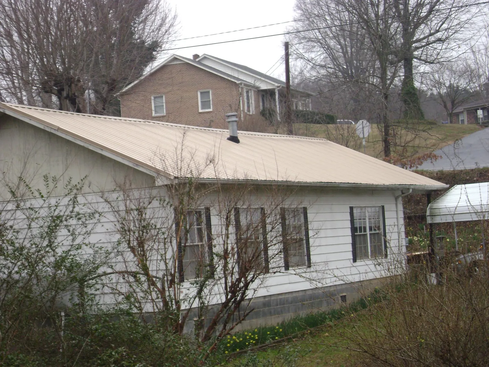 Tan metal roof on a white sided house set into a hillside — Commercial Roofing by Roofing Brothers in The Villages